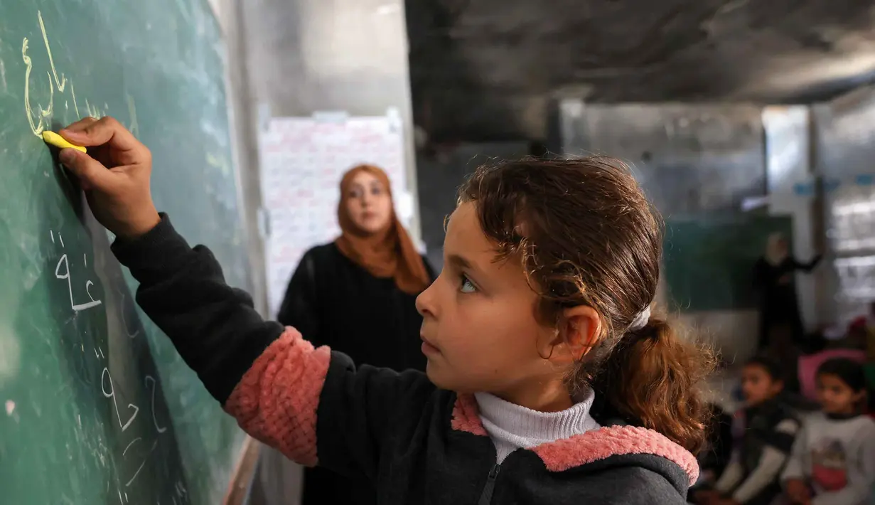 Ada lebih dari 658.000 anak usia sekolah kehilangan akses ke pendidikan formal selama lebih dari dua tahun akademik berturut-turut. Tampak dalam foto, seorang anak pengungsi Palestina menulis di papan tulis selama pelajaran di dalam tenda di Sekolah Mada, kamp pengungsi Jabalia, Jalur Gaza Utara pada 13 April 2026. (Omar AL-QATTAA/AFP)