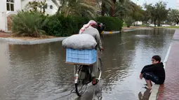 Seorang pria mengendarai sepeda di jalan banjir usai badai hujan, Abu Dhabi (9/3/2016 ). Akibat hujan lebat ini, sekolah diliburkan dan penerbangan ditunda. (AFP Photo)