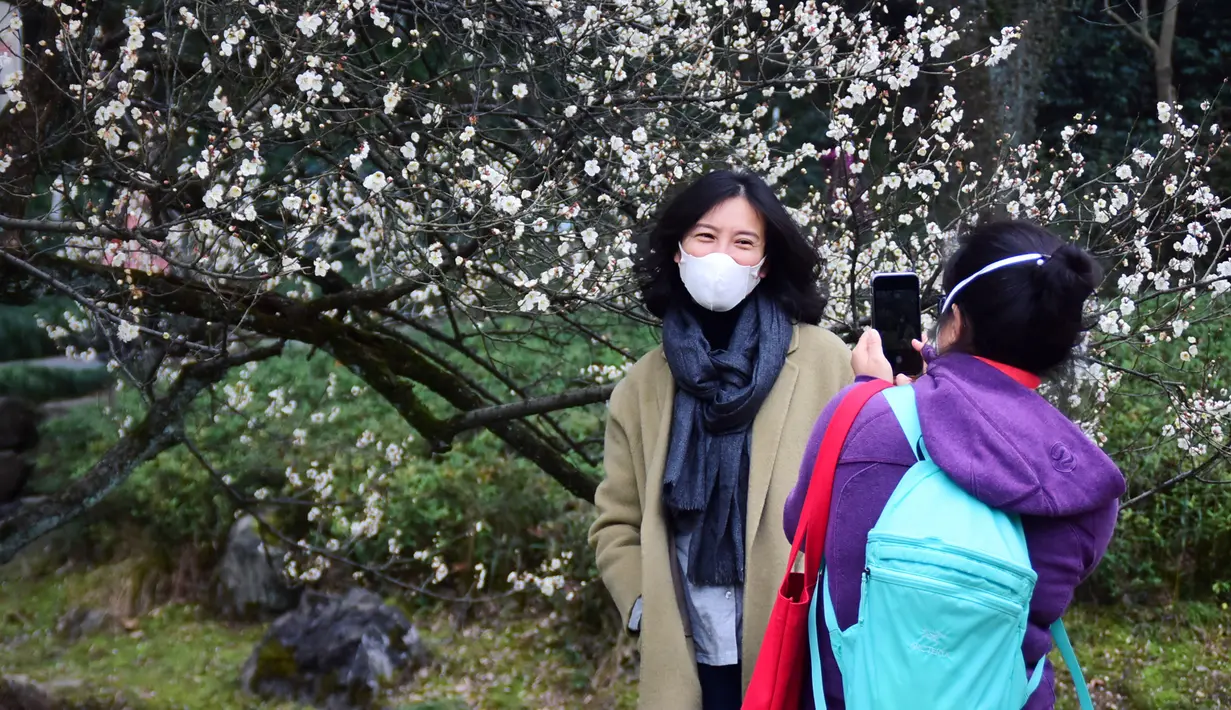 Seorang wanita berfoto di taman botani Hangzhou, Provinsi Zhejiang, China (19/2/2020). Sebagai upaya pencegahan coronavirus baru, kawasan indah tersebut telah menetapkan batas jumlah pengunjung saat ini dan semua yang memasuki kawasan itu diwajibkan mengenakan masker. (Xinhua/Zheng Mengyu)