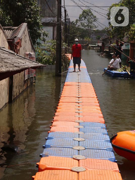 Warga berjalan melintasi jembatan apung saat banjir melanda Perumahan Periuk Damai, Tangerang, Banten, Selasa (23/2/2021). Adanya jembatan apung mempermudah warga saat melintasi banjir setinggi 2,5 meter di tempat tersebut. (Liputan6.com/Angga Yuniar)