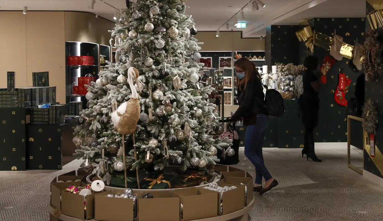 Seorang wanita yang mengenakan masker terlihat di samping pohon Natal di pusat perbelanjaan Harrods, London, Inggris, 2 Desember 2020. Sistem baru seiring berakhirnya karantina wilayah COVID-19 membagi Inggris ke dalam area-area dengan tingkat aturan pembatasan yang berbeda. (Xinhua/Han Yan)