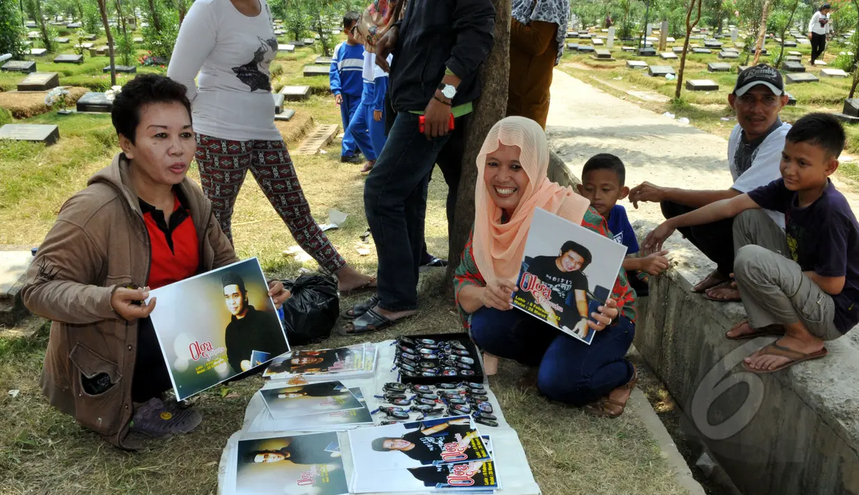 Seorang pedagang menunjukkan poster dagangannya yang bergambar Olga Syahputra di TPU Malaka, Jakarta, Selasa (31/3/2015). Empat hari pascakepergian komedian Olga, antusiasme masyarakat berkunjung ke makam masih tinggi. (Liputan6.com/Panji Diksana)