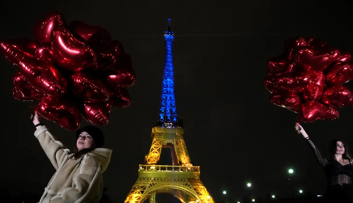 Para turis berpose dengan balon saat Menara Eiffel diterangi dengan warna-warna khas Ukraina untuk menandai peringatan satu tahun invasi Rusia ke negara tersebut, di Paris, Kamis, 23 Januari 2023. Pada 24 Februari 2022 lalu Rusia menginvasi Ukraina dan menandai puncak eskalasi konflik kedua negara sejak 2014 silam. (AP Photo/Christophe Ena)