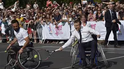 Presiden Prancis, Emmanuel Macron (tengah) bermain tenis menggunakan kursi roda bersama atlet, Michael Jeremiasz (kiri) di Paris, (24/6/2017). Kegiatan ini sebagai bentuk promosi Paris menjadi kandidat tuan rumah Olimpiade 2024. (AFP/Alain Jocard)