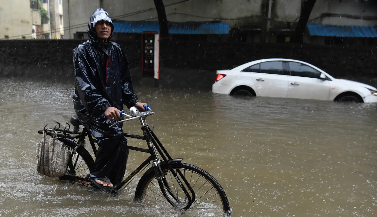 Seorang pria melintasi banjir dengan sepeda setelah hujan lebat di Mumbai, India (9/7). Mumbai dan daerah pinggiran lainnya telah mengalami hujan lebat semalaman yang mengakibatkan banjir. (AFP Photo/Indranil Mukherjee)