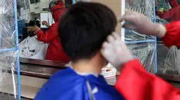 Pelanggan dipotong rambutnya oleh tukang cukur berpakaian alat pelindung diri (APD) yang tercermin di sebuah jendela di Manila, 8 Juni 2020. Filipina mengizinkan barbershop dan salon kecantikan beroperasi kembali dengan menerapkan langkah-langkah ketat pencegahan pandemi Covid-19. (AP/Aaron Favila)