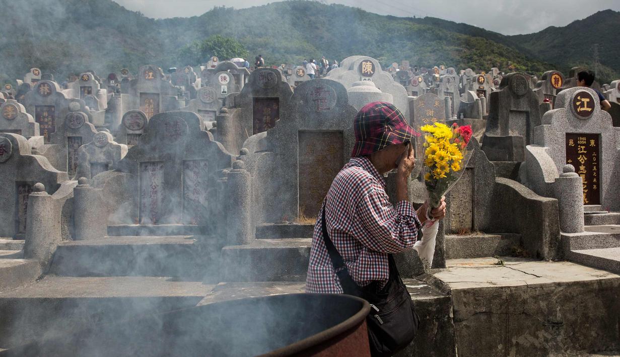 Seorang wanita membawa bunga selama festival Qingming di pemakaman di Hong Kong (5/4). Festival Qingming atau dikenal sebagai Hari Pembersihan Makam untuk menghormati orang yang dicintainya yang telah tiada. (AFP Photo/Isaac Lawrence)