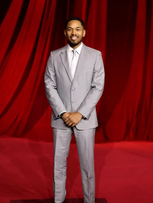 Kelvin Harrison Jr. mengenakan setelan wol abu-abu dengan kemeja poplin abu-abu muda dan dasi satin abu-abu muda. Sepatu boots kulit hitam yang disikat. [Prada]