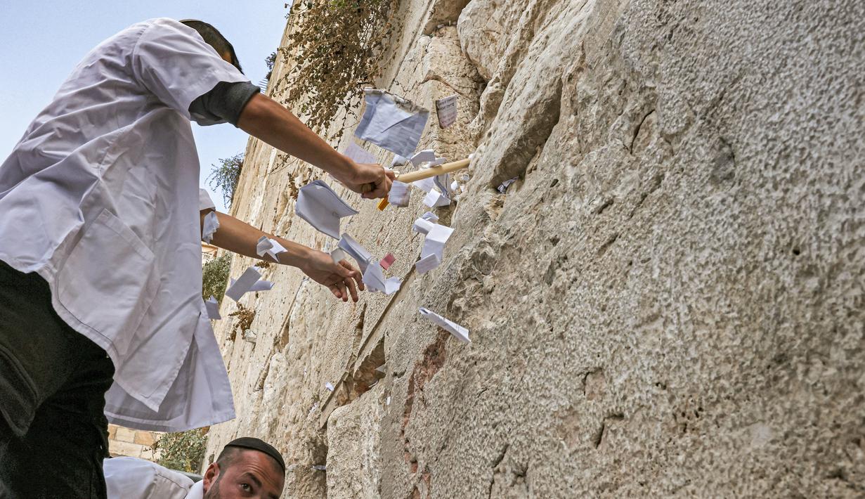 Pekerja pemeliharaan di Tembok Barat, situs paling suci di mana orang Yahudi diizinkan untuk berdoa, melakukan pembersihan untuk menghilangkan dari celah-celah pesan agama dan doa yang tertulis di selembar kertas yang ditinggalkan oleh ribuan jemaah sebelumnya, di kota tua Yerusalem pada 20 September 2022. (AFP/Ahmad Gharabli)