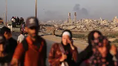 Asap membubung di atas bangunan-bangunan yang hancur saat warga Palestina meninggalkan kota Gaza ke arah selatan dengan membawa barang-barang mereka, melalui jalan pesisir dekat kamp pengungsi Nuseirat di bagian tengah Jalur Gaza, pada 12 September 2025. (Eyad BABA/AFP)