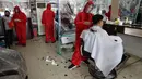 Tukang cukur mengenakan alat pelindung diri (APD) saat memotong rambut pelanggan di sebuah tempat pangkas rambut di Manila, 8 Juni 2020. Filipina mengizinkan barbershop dan salon kecantikan beroperasi kembali dengan menerapkan langkah-langkah ketat pencegahan pandemi Covid-19. (AP/Aaron Favila)