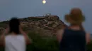 Pengunjung menyaksikan pemandangan bulan purnama hampir penuh yang menampakkan diri di langit Kuil Poseidon kuno di Cape Sounion, sekitar 70 kilometer sebelah tenggara Athena, Yunani (2/8/2020). (Xinhua/Marios Lolos)