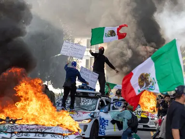 Pengunjuk rasa melambaikan bendera dari atas mobil yang rusak saat bentrok dengan penegak hukum di jalan-jalan di sekitar gedung federal selama protes setelah operasi imigrasi federal di Los Angeles, California, Amerika Serikat pada 8 Juni 2025. (RINGO CHIU/AFP)