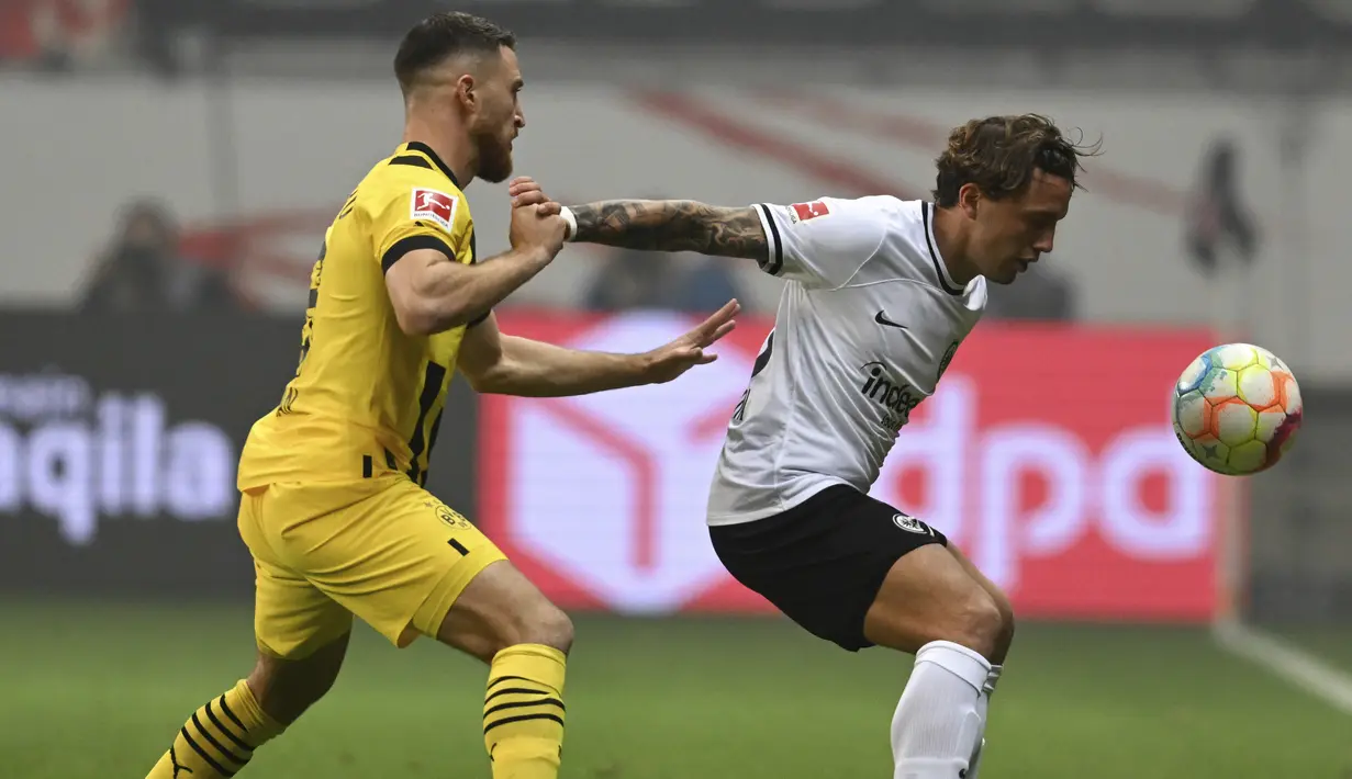 <p>Bek Eintracht Frankfurt, Luca Pellegrini berebut bola dengan gelandang Borussia Dortmund Salih Ozcan pada laga pekan ke-12 Bundesliga Jerman 2022/2023 di Deutsche Bank Park, Minggu (30/10/2022) dini hari WIB. Borussia Dortmund menang tipis 3-2 atas tuan rumah Eintracht Frankfurt. (Arne Dedert/dpa via AP)</p>