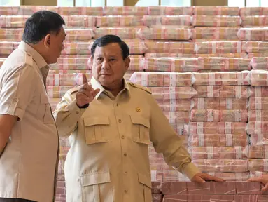 Presiden Prabowo Subianto (tengah) berbicara dengan Jaksa Agung Sanitiar Burhanuddin (kanan) dan Menteri Pertahanan Indonesia Sjafrie Sjamsoeddin di samping tumpukan uang kertas rupiah Indonesia senilai 800 juta USD di gedung Kejaksaan Agung Republik Indonesia, Jakarta, Senin 20 Oktober 2025. (BAY ISMOYO/AFP)