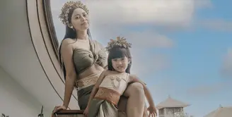Rachel kompak mengenakan pakaian khas perempuan Bali bersama putrinya, Chava. Chava menggemaskan mengenakan atasan nude dipadu obi dan rok lilit hijaunya. Lengkap dengan aksesori bros dan rambut. (@rachelvennya)