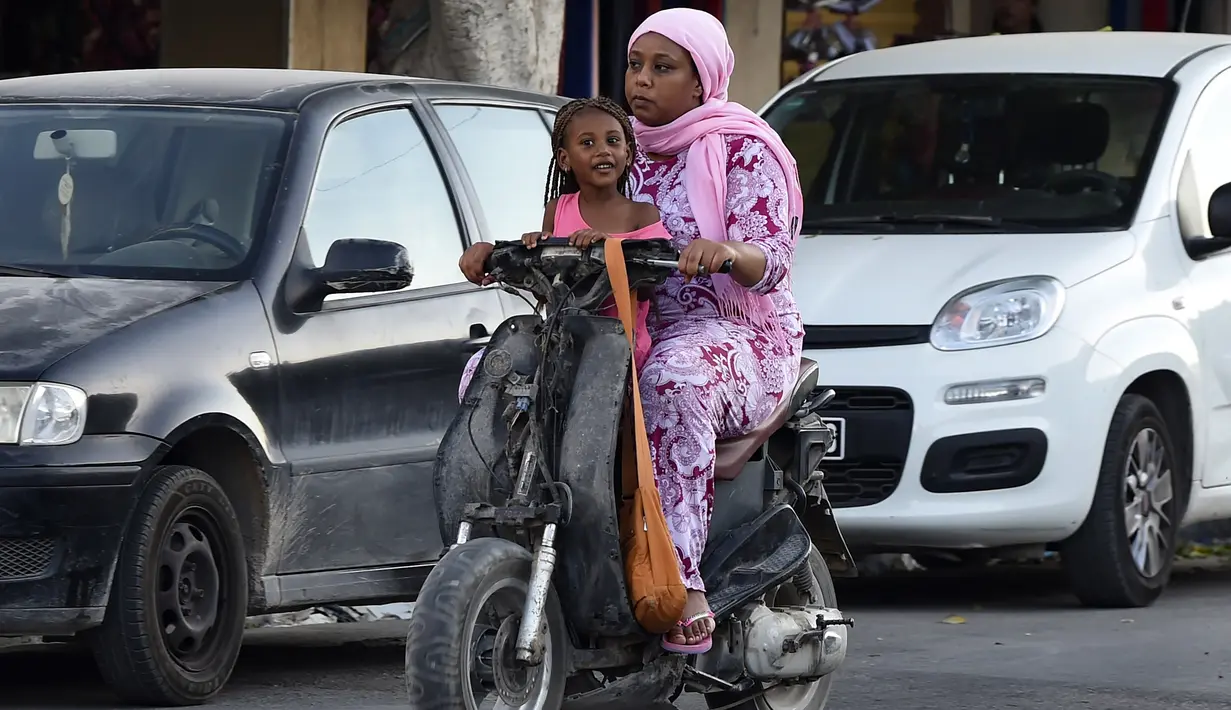 Seorang perempuan Tunisia dan anaknya menaiki skuter ketika kasus baru infeksi Corona di sana melonjak, di kota Gabes, Rabu (27/8/2020). Tunisia pada 25 Agustus 2020 melaporkan peningkatan tertinggi kasus baru Covid-19 dibandingkan minggu sebelumnya. (FETHI BELAID/AFP)