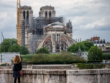 Seorang wanita mengamati Katedral Notre-Dame yang tengah dipugar di Paris, Prancis, Senin (27/4/2020). Renovasi Katedral Notre-Dame dilanjutkan kembali setelah sempat dihentikan sejak 17 Maret lalu akibat epidemi COVID-19. (Xinhua/Aurelien Morissard)