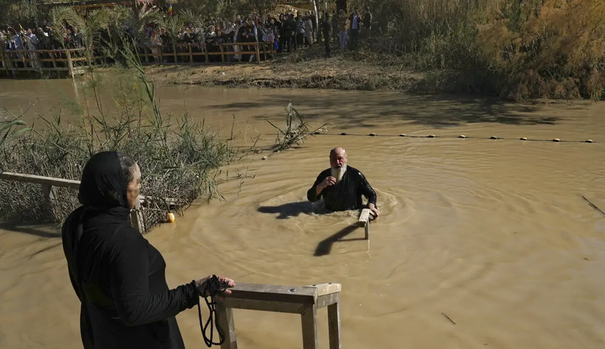 Seorang peziarah Kristen Ortodoks membenamkan dirinya ke Sungai Yordan saat upacara pembaptisan pada perayaan Epiphany di Qasr el Yahud, dekat kota Yerikho, Tepi Barat, 18 Januari 2022. Sungai Yordan dipercaya menjadi tempat di mana Yesus dibaptis. (AP Photo/Mahmoud Illean)