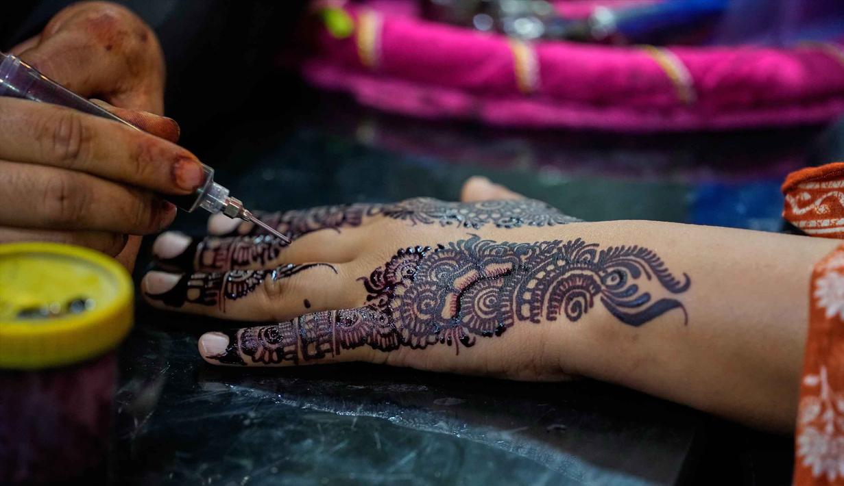 Seorang ahli kecantikan melukis 'Henna' tradisional di tangan pelanggan untuk perayaan Idul Fitri, yang menandai berakhirnya bulan suci Ramadan, di Rawalpindi, Pakistan, Rabu 18 Maret 2026. (AP Photo/Anjum Naveed)