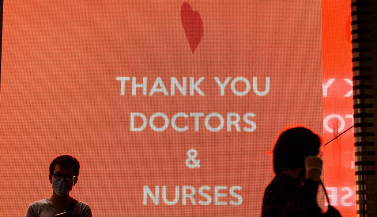 Pejalan kaki memakai masker wajah sebagai tindakan pencegahan terhadap virus corona COVID-19 ketika mereka berjalan melewati papan pajangan elektronik dengan pesan terima kasih kepada dokter dan perawat di Hong Kong (13/5/2020). (AFP/Anthony Wallace)