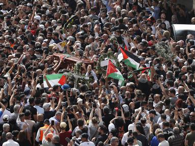 Orang-orang Palestina mengibarkan bendera nasional saat membawa peti mati jurnalis Al-Jazeera Shireen Abu Akleh yang tewas tertembak selama prosesi pemakamannya di dekat Gerbang Jaffa, salah satu gerbang utama Kota Tua Yerusalem, 13 Mei 2022. Shireen Abu Akleh yang merupakan jurnalis senior berusia 51 tahun itu terkena tembakan di kepala ketika meliput serangan Israel di Kota Jenin, di wilayah Tepi Barat yang diduduki pada 11 Mei 2022 lalu. (Ahmad GHARABLI / AFP)