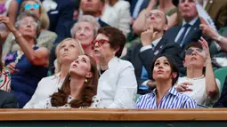 Kate Middleton dan Meghan Markle saat menyaksikan kejuaraan  tenis Wimbledon di London, Inggris, (14/7). Meghan mengenakan kemeja longgar bergaris biru putih serta celana putih. Kate memakai mini dress bermotif hitam putih. (AP Photo/Andrew Couldridge)