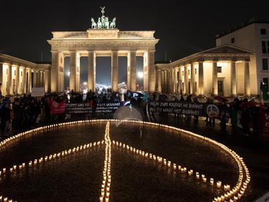 Para aktivis meletakkan lilin yang membentuk tanda perdamaian di depan Gerbang Brandenburg, menjelang peringatan satu tahun invasi Rusia ke Ukraina, di Berlin, Jerman, Kamis (23/2). Setahun sudah invasi Rusia ke Ukraina berlangsung. Namun, hingga kini belum ada tanda-tanda Rusia ingin mengakhiri agresi dan berdamai. (Paul Zinken/dpa via AP)