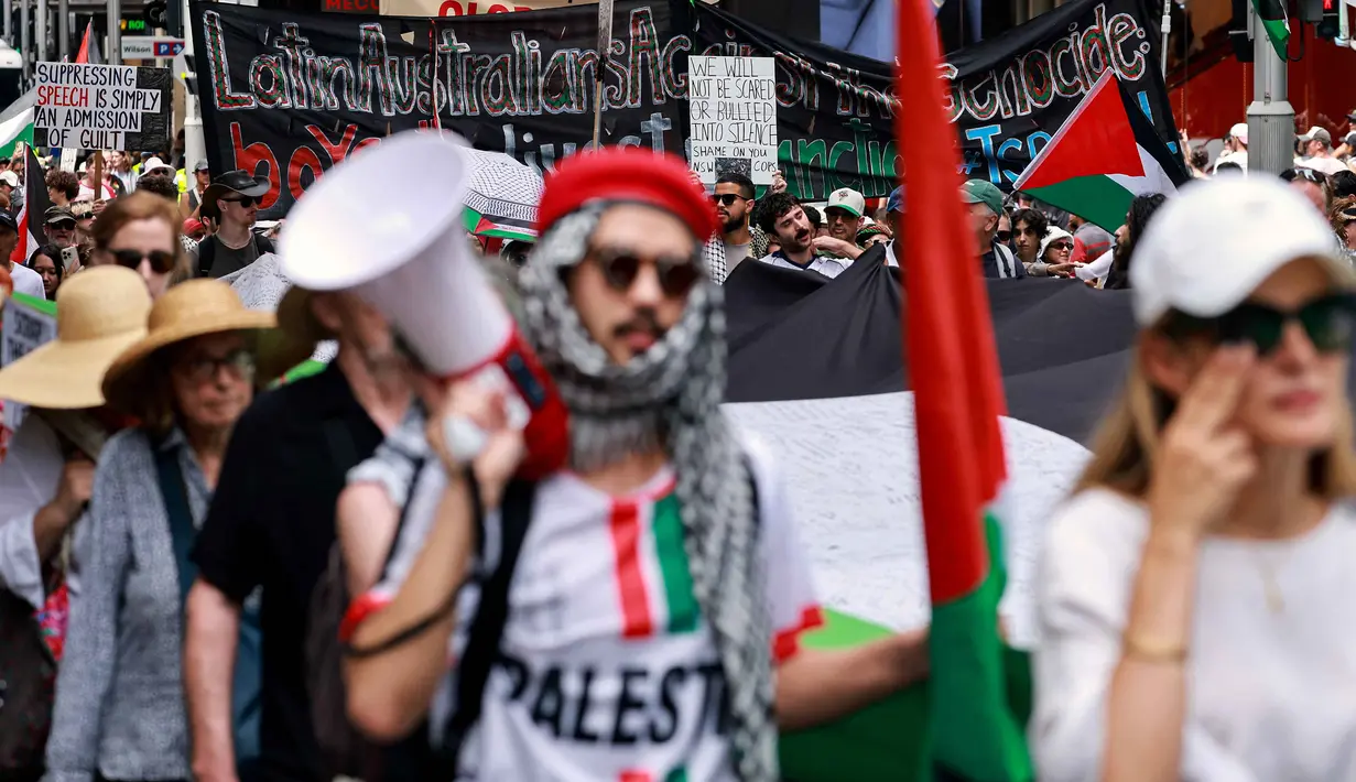 Aksi ini merupakan bagian dari gelombang protes berkelanjutan di Australia yang menuntut keadilan bagi warga Palestina di kota Gaza. Tampak dalam foto, para demonstran pro-Palestina membawa bendera, spanduk, dan plakat saat mereka berbaris berunjuk rasa di jalanan kota Sydney, Australia, Minggu 22 Februari 2026. (DAVID GRAY/AFP)