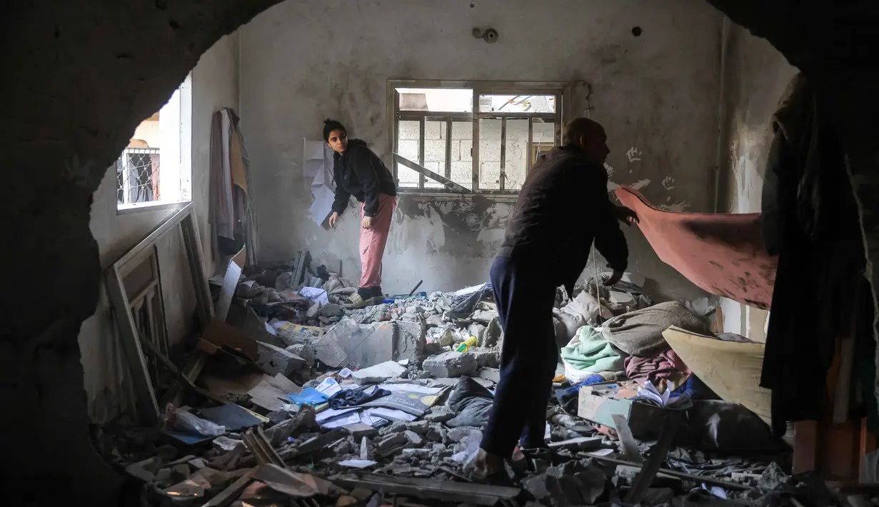 Warga Palestina menyelamatkan barang-barang dari sebuah rumah setelah serangan militer Israel terhadap rumah keluarga al-Houli, di mana empat orang dilaporkan tewas, di sebelah barat Deir al-Balah, di Jalur Gaza tengah, pada Jumat 16 Januari 2026. Jumlah korban tewas akibat serangan Israel di Jalur Gaza terus bertambah. (BASHAR TALEB/AFP)