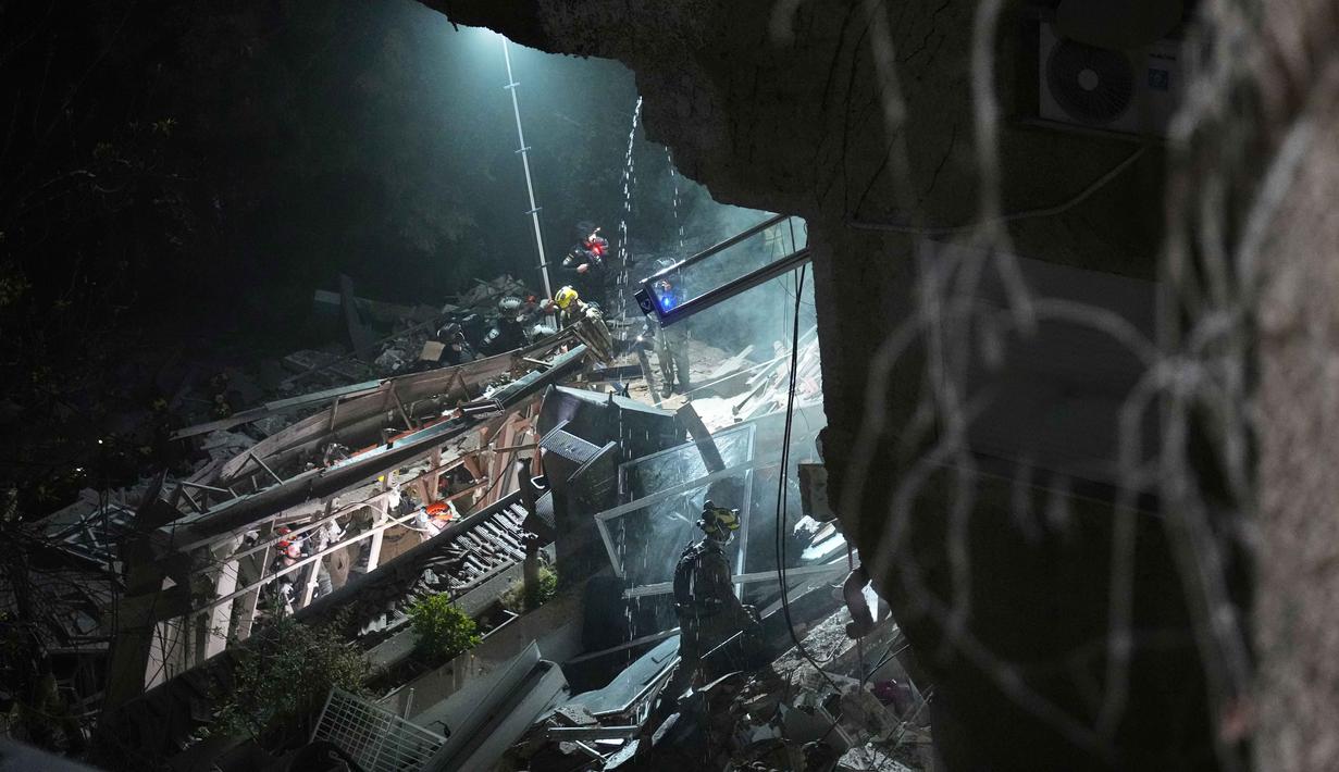 Puluhan personel keamanan dan tim darurat telah dikerahkan ke lokasi untuk melakukan pencarian dan penyelamatan intensif di reruntuhan bangunan. Tampak dalam foto, pasukan keamanan Israel dan tim penyelamat melakukan upaya pencarian korban di tengah reruntuhan bangunan tempat tinggal yang dihantam rudal Iran di Haifa, Israel, Minggu, 5 April 2026. (AP Photo/Ariel Schalit)