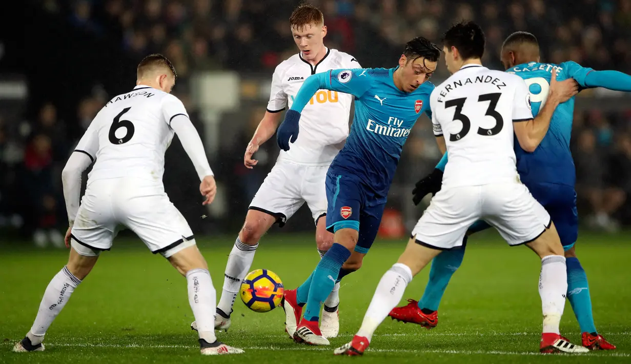 Pemain Arsenal, Mesut Ozil berusaha merebut bola dengan kawalan pemain Swansea City dalam laga pekan ke-25 Premier League 2017-2018 di Liberty Stadium, Selasa (30/1). Arsenal dipaksa menyerah Swansea City 1-3. (Nick Potts/PA via AP)