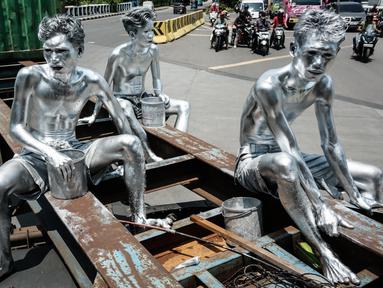 Foto yang diambil pada 7 April 2025 ini menunjukkan manusia silver Keris Munandar (kanan), saudaranya Ari Munandar (kiri), dan tetangganya Riyan Ahmad Fazriyansah menumpang di bagian belakang truk kontainer untuk mencapai persimpangan di Jakarta. (Yasuyoshi CHIBA/AFP)