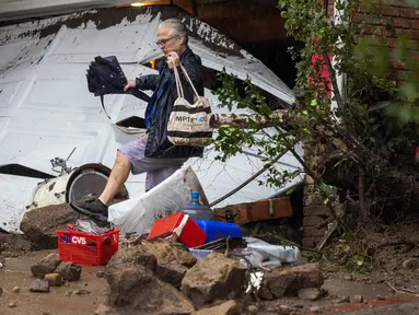 Seorang pria melangkah di atas puing-puing di dekat garasi yang dihantam tanah longsor dan banjir bandang di lingkungan pemukiman, California, pada 5 Februari 2024. (DAVID MCNEW/AFP)