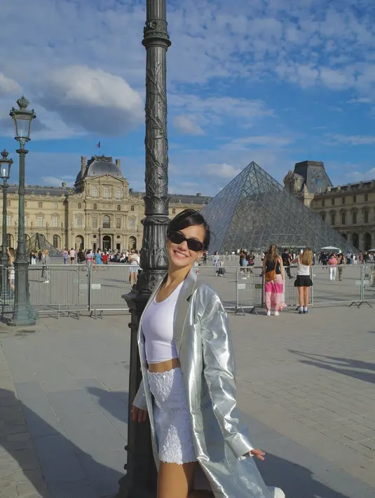Gaya unik Pevita Pearce di Paris mengenakan tank top putih dipadu mini skirt bernuansa senada, ditumpuknya dengan trench coat silver yang berkilauan. [Foto: Instagram/pevpearce]