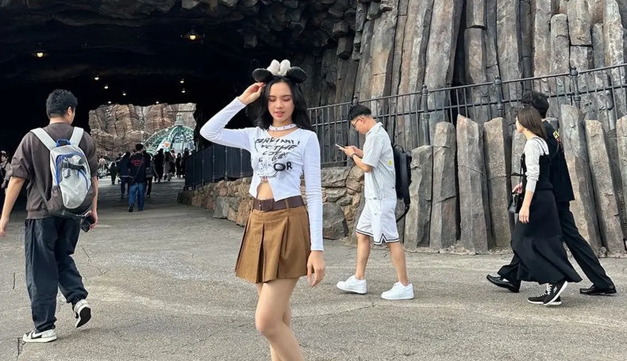 Jalan-jalan di Disney, Lyodra memilih mengenakan atasan lengan panjang putih dipadukan mini skirt pleated coklat dan sabuknya serta sneakersnya. Tampil cute dengan bando Minnie Mousenya. [@lyodraofficial]