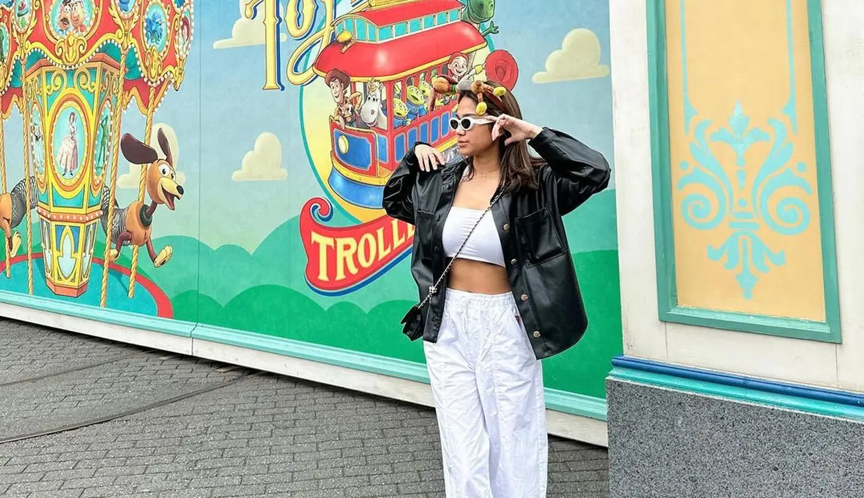 Gaya Azizah Salsha berlibur ke theme park. Ia mengenakan cropped top dan celana panjang putih, ditumpuknya dengan jaket kulit hitam. Gayanya semakin gemas dengan bando karakter, sunglasses, dan sling bag hitam. [Foto: Instagram/azizahsalsha_]