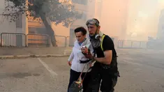 Petugas layanan darurat mengevakuasi seorang wanita dari rumahnya di kota utara Israel, Haifa, Kamis (24/11). Sekitar 80 ribu warga Israel diperintahkan untuk dievakuasi akibat kebakaran hutan yang melanda seluruh wilayah tersebut. (REUTERS/Rami Shlush)