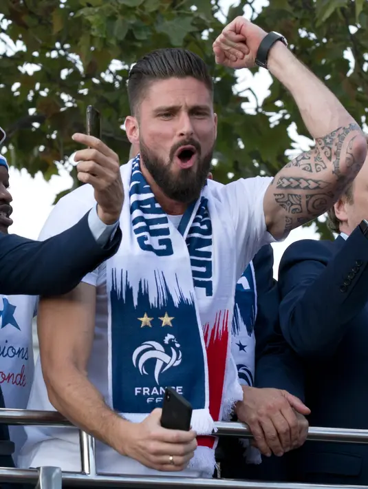 Striker timnas Prancis, Olivier Giroud berada di atas bus beratap terbuka saat parade merayakan juara Piala Dunia 2018 di sepanjang Champs Elysees, Paris, Senin (16/7). Prancis meraih trofi Piala Dunia kedua usai mengalahkan Kroasia. (AP/Claude Paris)