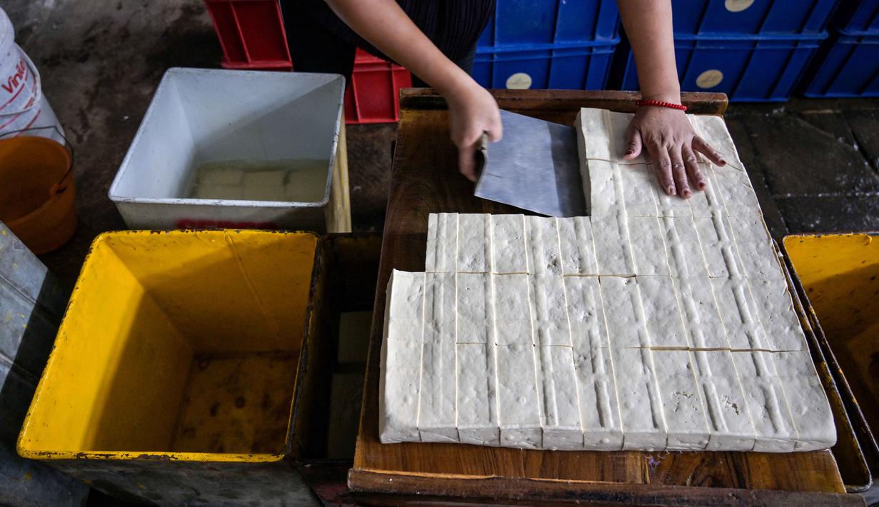 Seorang pekerja memotong tahu di sebuah pabrik, Surabaya, Jawa Timur pada Kamis 5 Februari 2026. (JUNI KRISWANTO/AFP)