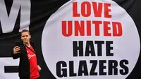 Seorang pendukung mengambil foto di samping spanduk anti-Glazer saat para pengunjuk rasa berkumpul di luar stadion Old Trafford untuk berdemonstrasi menentang pemilik Manchester United itu. (ANTHONY DEVLIN / AFP)