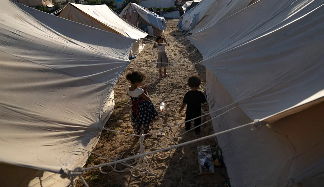 Anak-anak Palestina yang mengungsi akibat pemboman Israel di Jalur Gaza berjalan di tenda kamp yang disediakan UNDP di Khan Younis, Kamis (19/10/2023). (AP Photo/Fatima Shbair)
