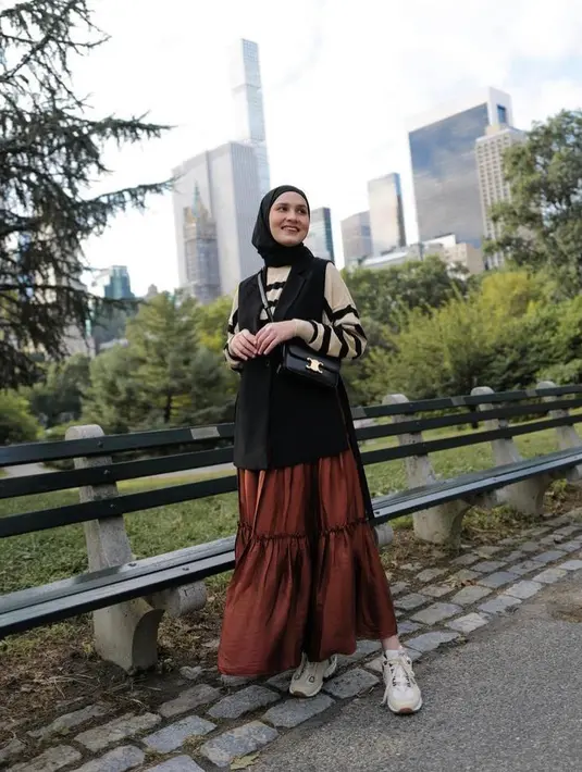 Kombinasi striped long sleeve top sebagai inner dengan sleeveless outer warna hitam, hijab warna senada,  dan tiered skirt warna coklat juga tak kalah menarik. Sempurnakan OOTD-mu dengan sling bag dan sneakers putih. (Instagram/dwihandaanda).