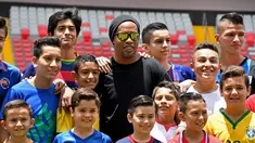 Mantan bintang sepak bola Brasil Ronaldinho berpose dengan anak-anak Kosta Rika sebelum pertandingan persahabatan melawan mantan pemain Kosta Rika di Stadion Nasional di San Jose, (4/8). (AFP Photo/Ezequiel Becerra)