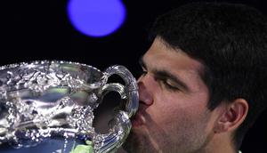 Carlos Alcaraz mencium piala usai berhasil menjuarai Australian Open 2026 setelah menaklukkan Novak Djokovic dalam laga sengit yang dilangsungkan di Melbourne Park pada (1/2/2026) sore WIB. (AFP/Martin Keep)