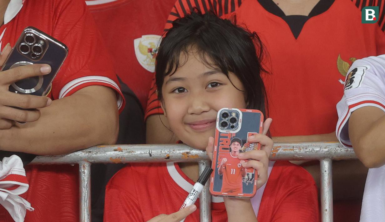 Suporter cilik menunjukkan Handphone bergambar Rafael Struick saat menyaksikan secara langsung pertandingan Timnas Indonesia vs Jepang pada laga Grup C putaran ketiga Kualifikasi Piala Dunia 2026 Zona Asia di Stadion Utama Gelora Bung Karno, Jakarta, Jumat (15/11/2024). (Bola.com.M Iqbal Ichsan)