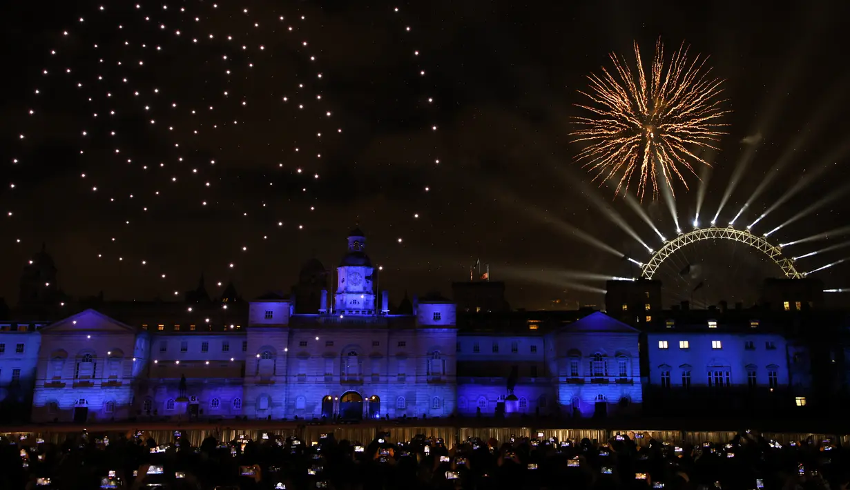 Orang-orang menonton tampilan lampu drone yang menampilkan mantan Ratu Elizabeth II Inggris dan kembang api dari Horse Guards Parade di pusat kota London untuk merayakan Tahun Baru pada Minggu, 1 Januari 2023. (AP Photo/David Cliff)