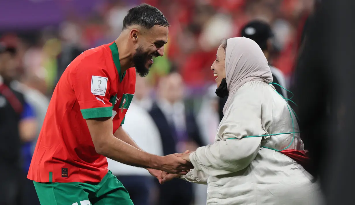 <p>Gelandang Maroko #17 Sofiane Boufal merayakan bersama ibunya setelah lolos ke semifinal dengan mengalahkan Portugal pada babak 8 besar Piala Dunia 2022 di Stadion Al-Thumama di Doha, Sabtu (10/12/2022). Pemain klub Prancis, Angers, itu berputar-putar berbagi kebahagiaan dengan keluarga. (KARIM JAAFAR / AFP)</p>