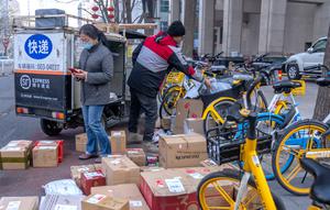 Seorang wanita mengambil paket dari kurir pengiriman di luar gedung perkantoran di Beijing, China, Senin (6/3/2023). Pejabat ekonomi China menyatakan keyakinannya bahwa mereka dapat memenuhi target pertumbuhan tahun ini sekitar 5 persen dengan menghasilkan 12 juta pekerjaan baru dan mendorong pengeluaran konsumen setelah berakhirnya kontrol antivirus yang membuat jutaan orang tetap di rumah. (AP Photo/Mark Schiefelbein)