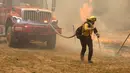 Seorang petugas pemadam kebakaran menarik selang untuk memadamkan api dekat Mariposa, California (23/7/2022). Api Oak yang bergerak cepat membakar di luar Taman Nasional Yosemite telah memaksa evakuasi, menghanguskan lebih dari 11.500 hektar dan telah menghancurkan beberapa rumah sejak mulai Jumat sore. (Justin Sullivan/Getty Images/AFP)